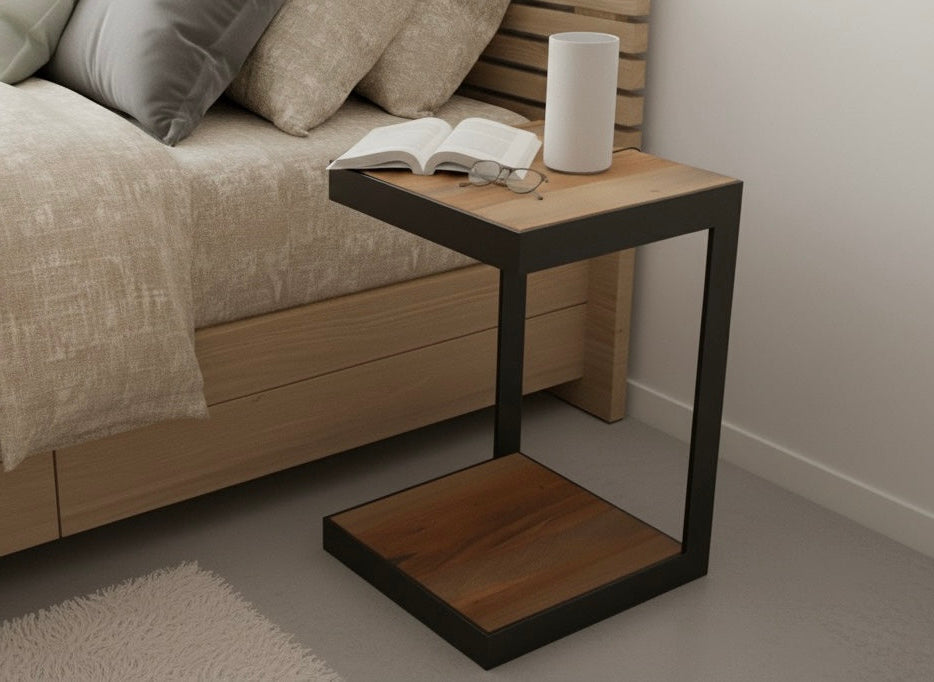 Wooden side table with a book and white cup next to a bed in a bedroom setting.