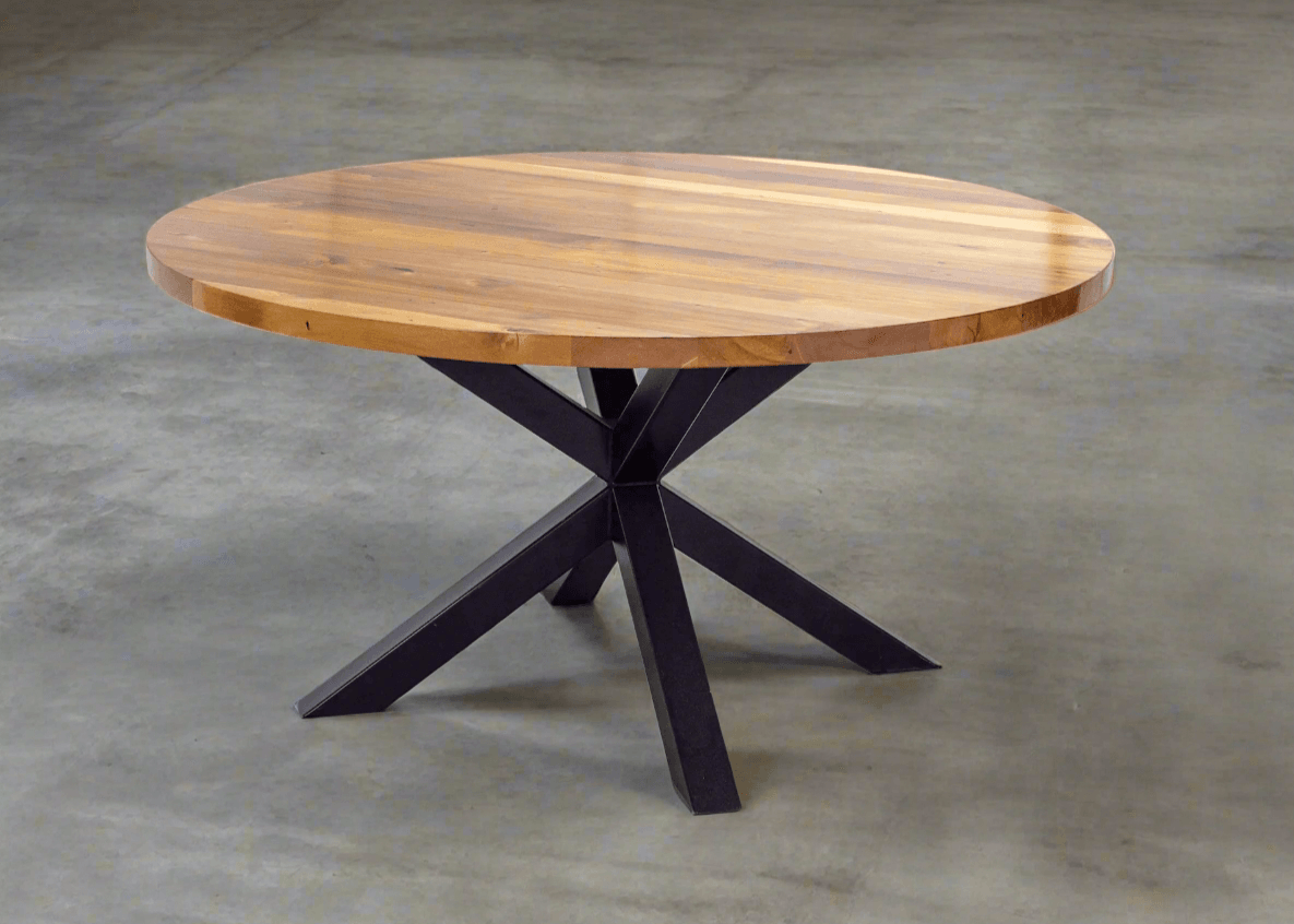 A round solid wood dining table with a smooth natural finish, shown in a contemporary dining area with chairs evenly spaced around its circular shape.
