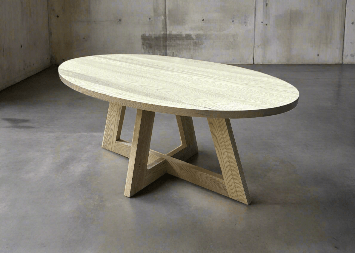 A handcrafted solid wood oval dining table with a smooth polished surface and gently curved ends, set in a contemporary dining room with complementary chairs.