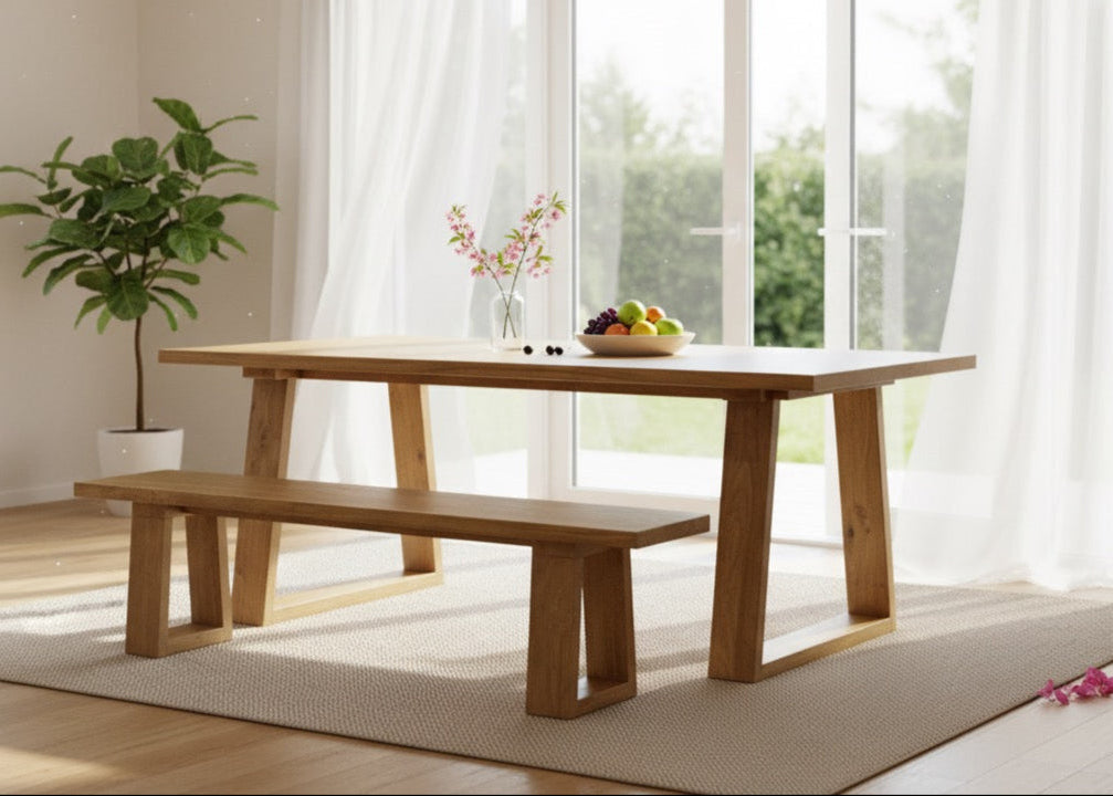 Wooden dining table with bench in a bright room with large windows.