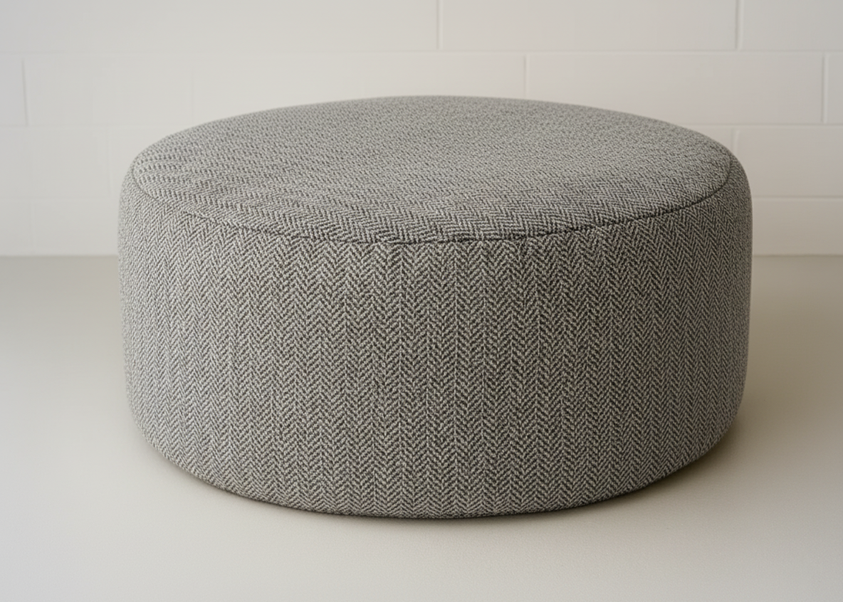 Gray textured ottoman on a white floor with a white wall background