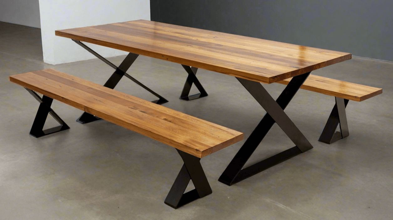 A large dining table featuring crossed X-shaped leg frames at each end and a thick wooden top, creating a modern architectural look in a spacious dining room.