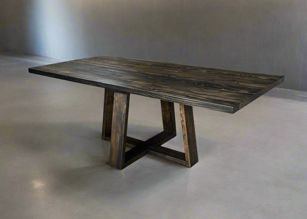 A large rectangular farmhouse-style dining table made of solid wood, supported by cross-shaped wooden trestle legs at each end, displayed in a warmly lit dining room.