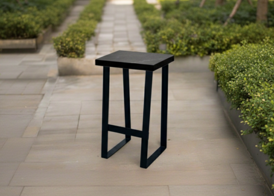 Black outdoor bar stool on a paved patio with greenery
