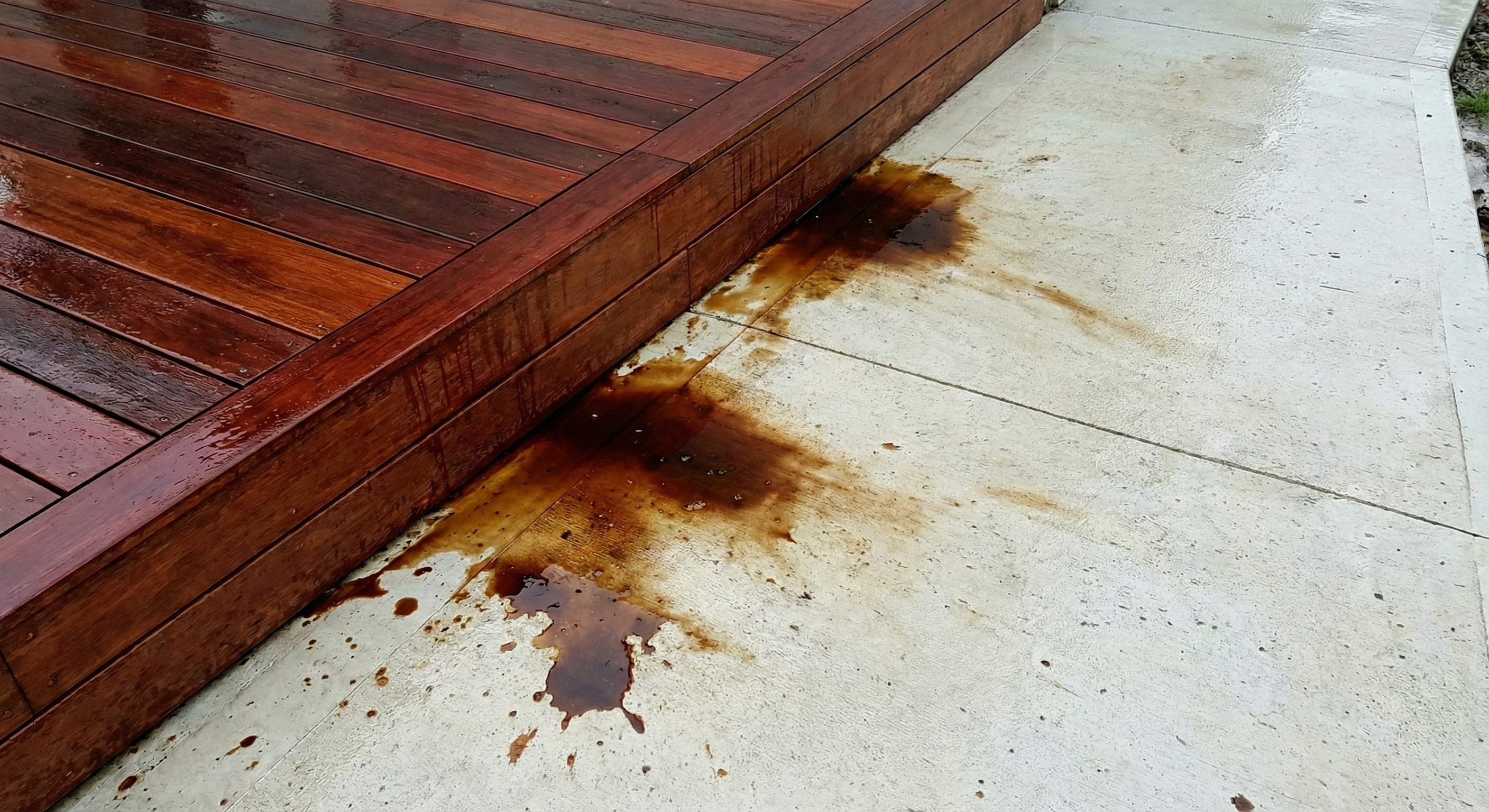 Wet Kwila deck bleeding reddish-brown tannins onto light concrete paving
