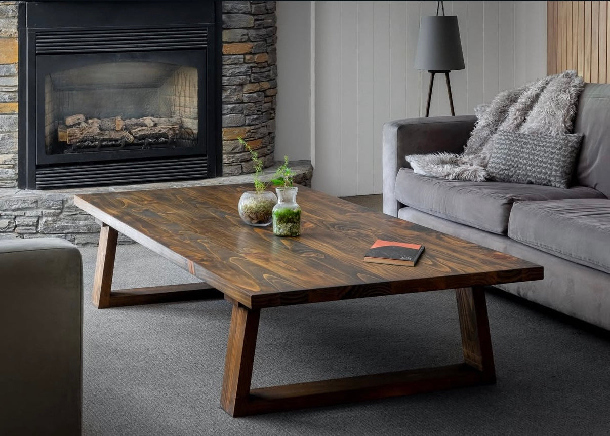 Wooden coffee table in a living room with a gray sofa and stone fireplace.