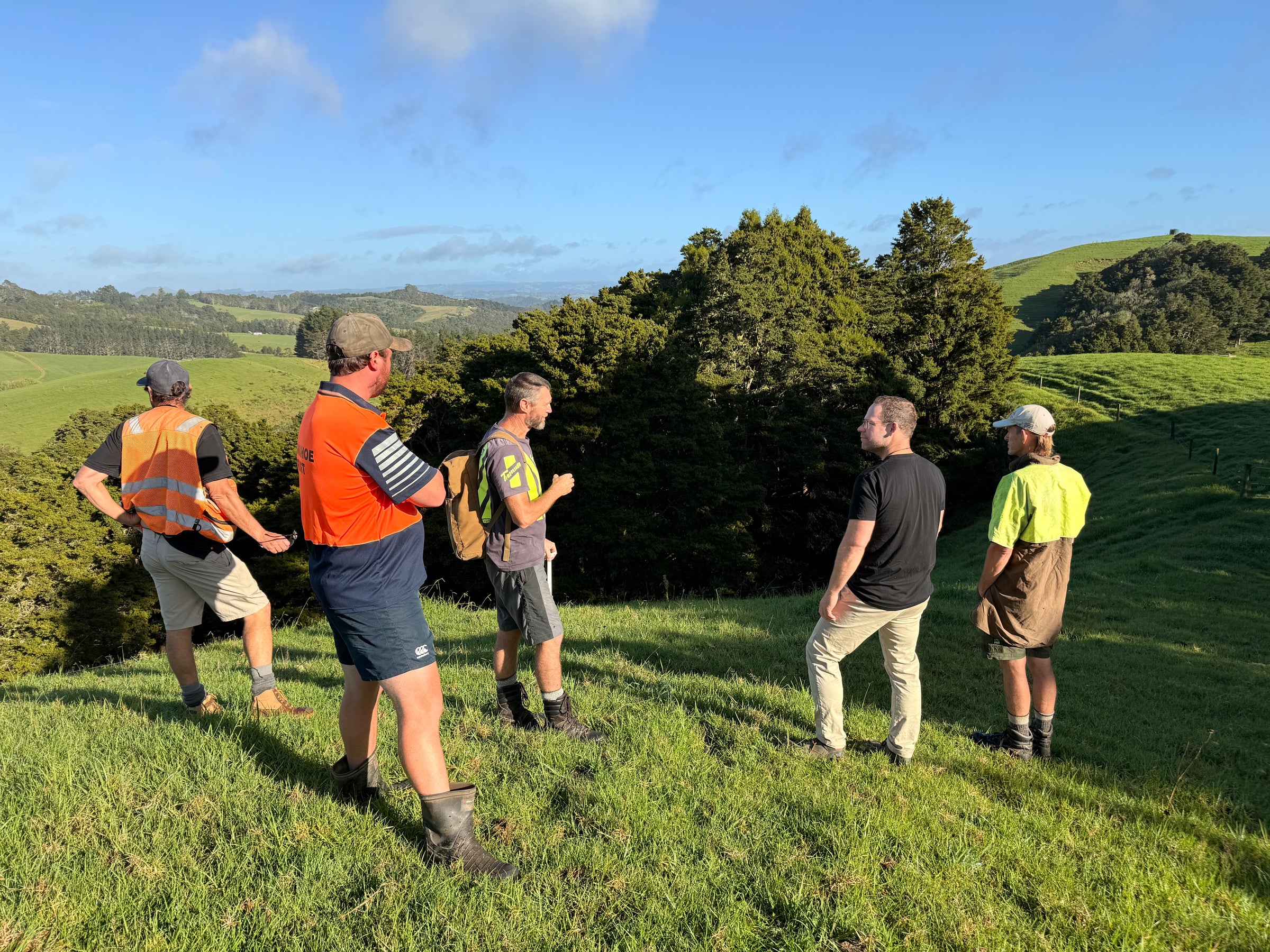 Five-person team standing on a Northland hilltop, rolling green farmland and native bush in the distance.