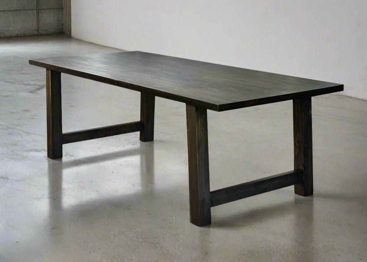A sleek farmhouse-style dining table crafted from solid wood, featuring straight modern legs and a spacious rectangular top, shown in a bright kitchen dining area with rustic décor accents.