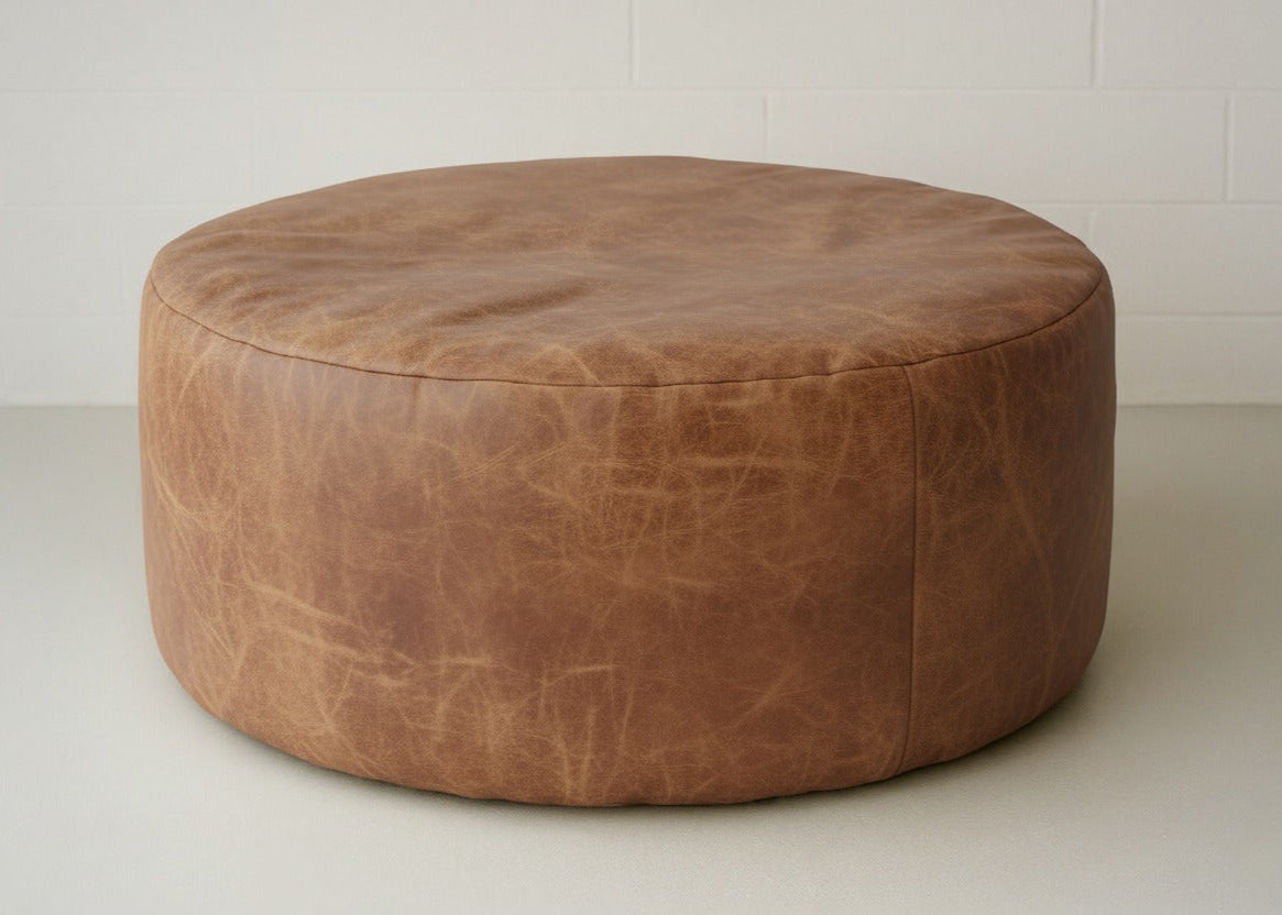 Brown leather ottoman on a white floor with a white wall background