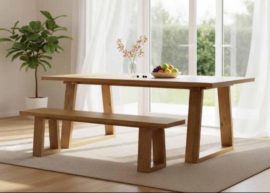 Wooden dining table with bench in a bright room with large windows.