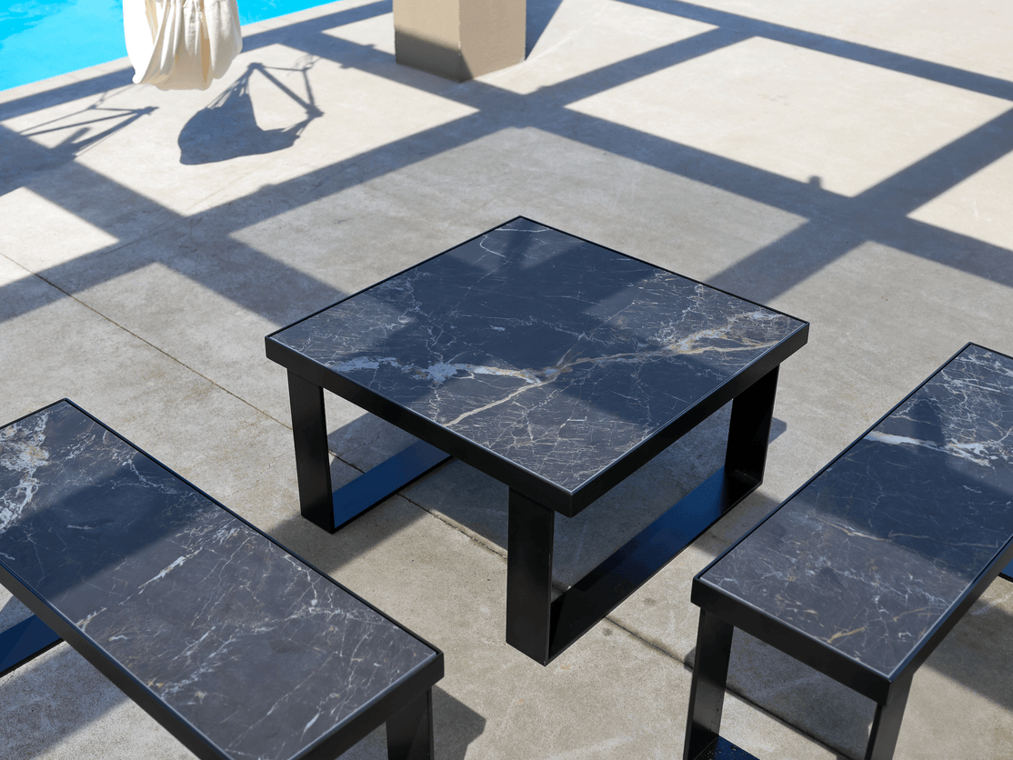 Black square outdoor tables with dark veined tops beside a pool