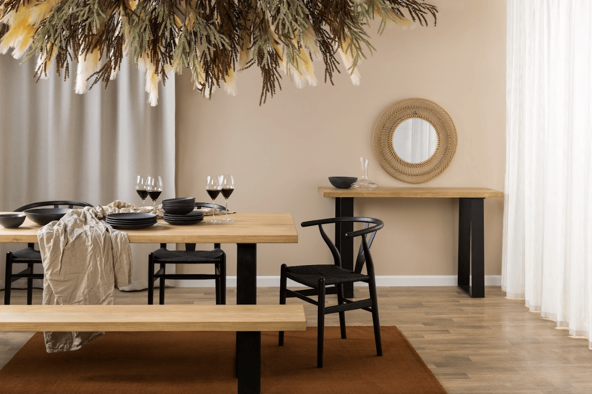  A handcrafted solid wood dining table with black powder-coated steel angled legs, shown with a matching wood bench in a contemporary dining room.