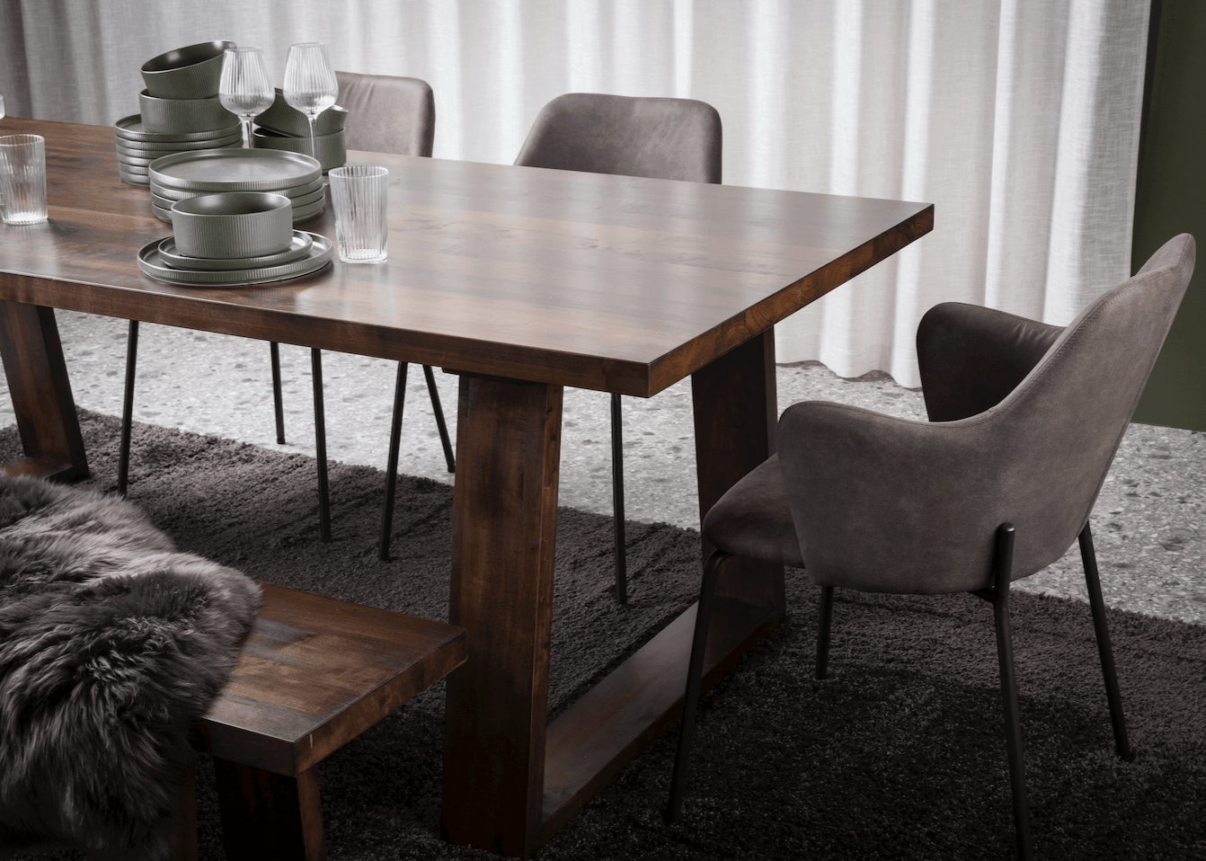 A solid wood dining table featuring uniquely angled wooden legs and a matching bench, showcasing natural timber grain in an airy modern dining space.