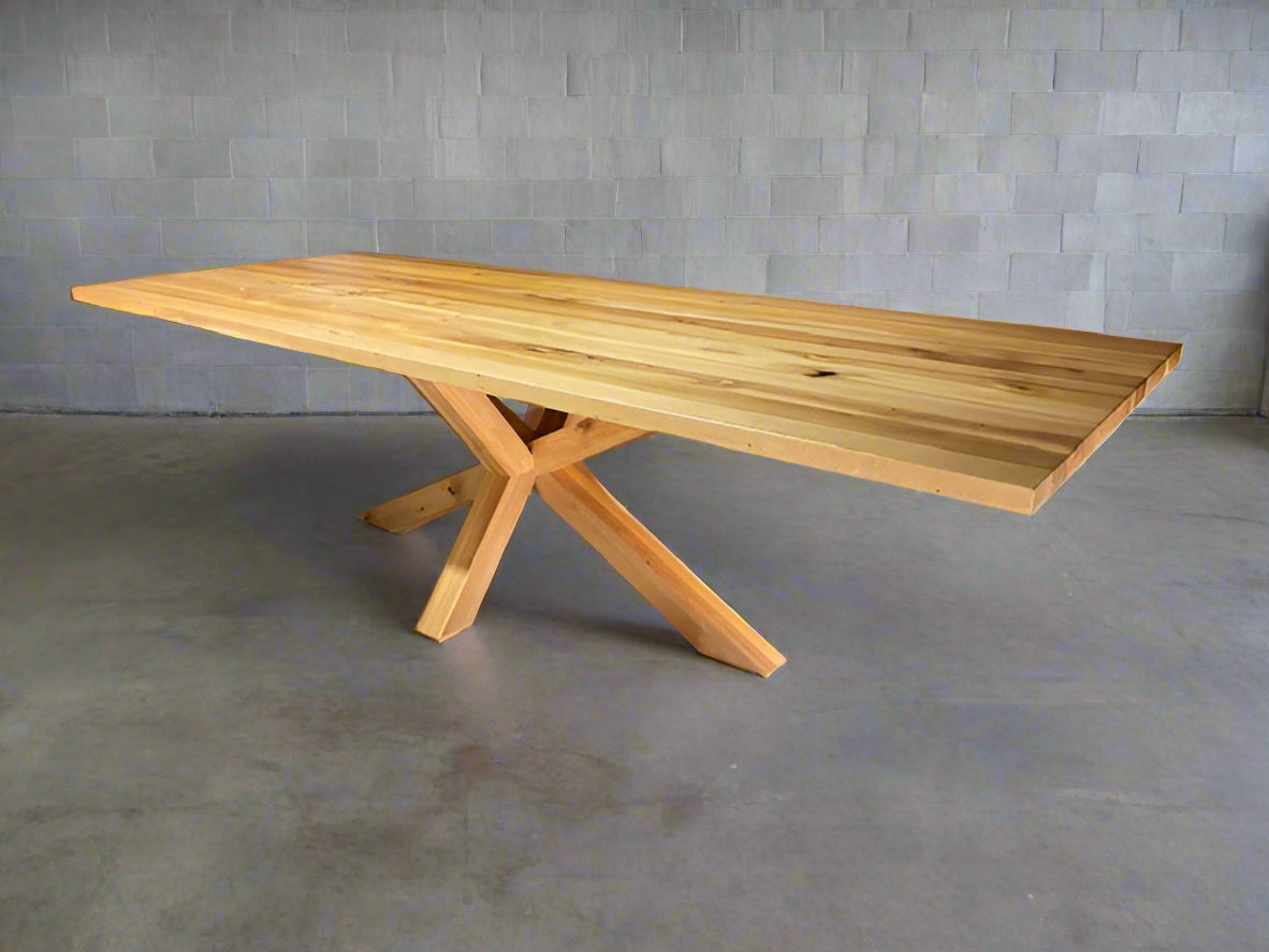 Wooden dining table with X-shaped legs on a gray floor and wall background