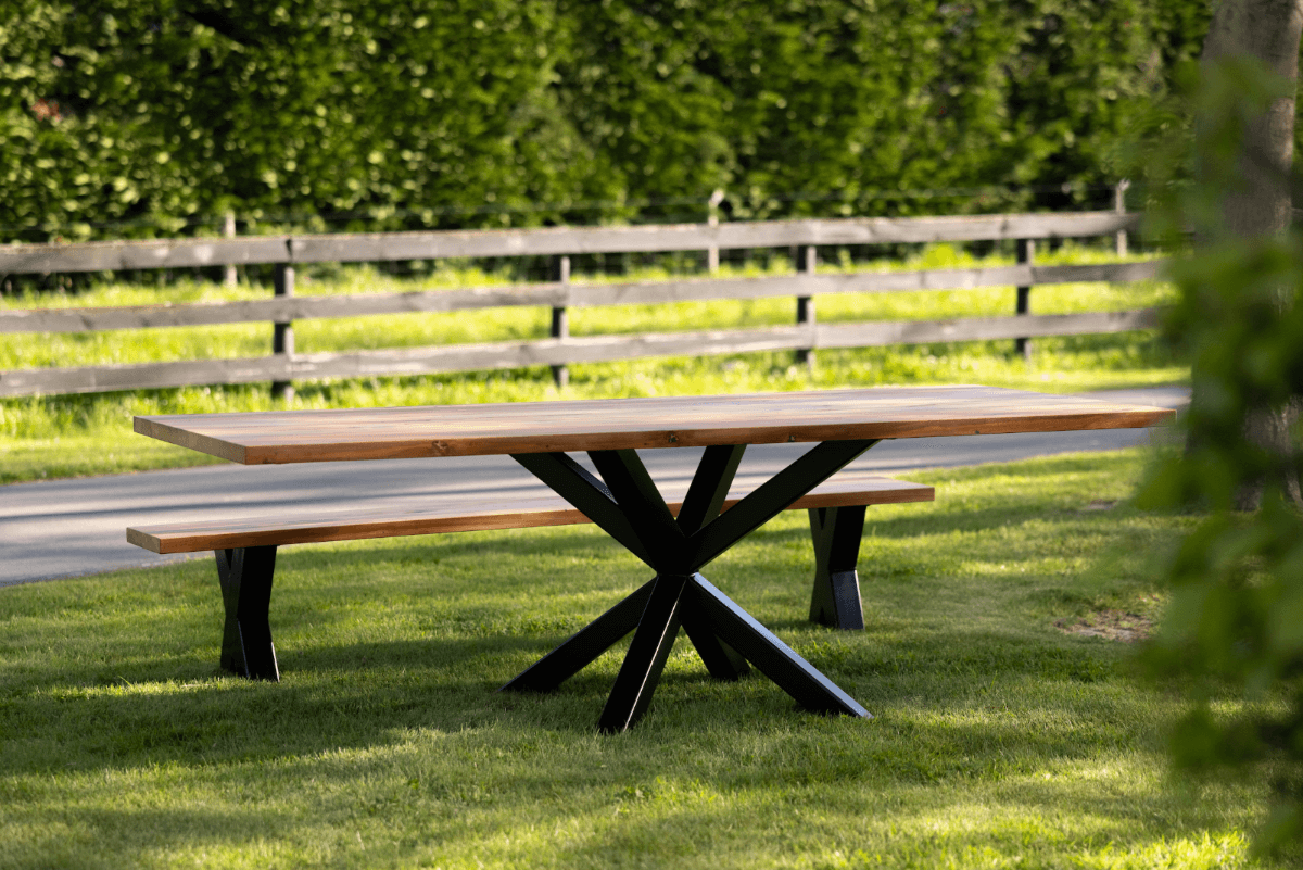 A modern dining table with a thick solid wood top and a black steel X-shaped pedestal base, surrounded by dining chairs in a contemporary home setting