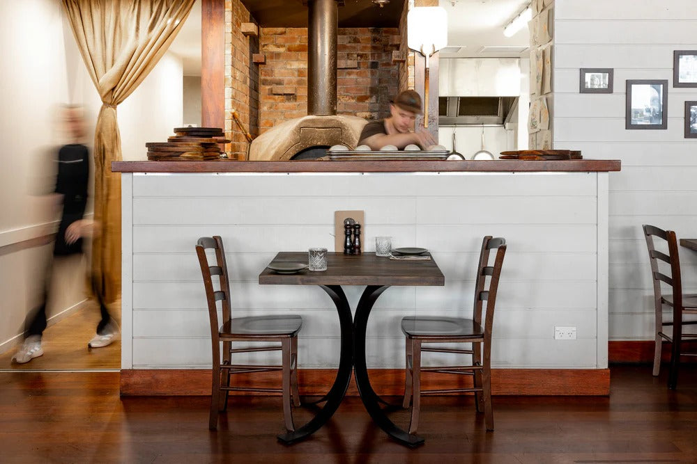Francesca’s Kitchen restaurant interior with timber table set near the open kitchen and brick pizza oven